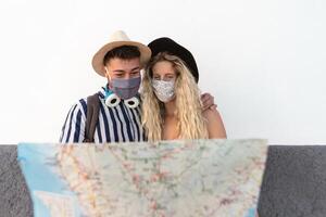 jovem casal vestindo face mascarar e segurando viagem mapa - Viajantes pessoas desfrutando primeiro viagem depois de corona vírus surto - reiniciar turismo e amor relação período de férias estilo de vida conceito foto