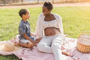 feliz brincalhão afro mãe e filho tendo Diversão dentro parque fazendo uma piquenique juntos - família amor conceito foto