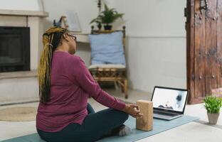 africano Senior mulher fazendo ioga virtual ginástica classe com computador portátil às casa - e-learning e pessoas bem estar estilo de vida conceito foto