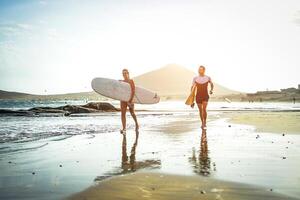 surfistas casal corrida juntos com pranchas de surf em a de praia às pôr do sol - Esportes amigos tendo Diversão surfar - viagem, feriados, esporte estilo de vida conceito foto