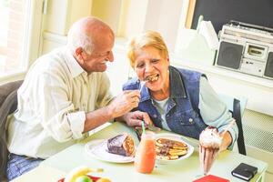 feliz idosos casal comendo panquecas dentro uma Barra restaurante - aposentado pessoas tendo Diversão desfrutando almoço juntos - conceito do idosos aposentado pessoa momentos - vintage filtro - suave foco em masculino face foto