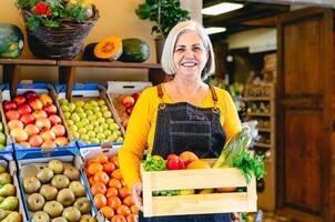 fêmea verdureiro trabalhando às a mercado segurando uma caixa contendo fresco frutas e legumes - Comida varejo conceito foto