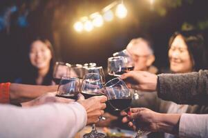 feliz família torcendo com vermelho vinho às reunião jantar dentro jardim - Senior tendo Diversão brindar taças de vinho e jantar juntos ao ar livre - pessoas e Comida estilo de vida conceito foto