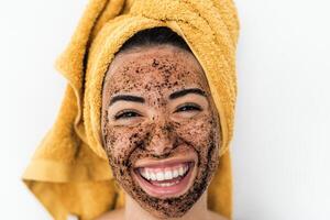 jovem sorridente mulher aplicando café esfregar mascarar em face - feliz menina tendo pele Cuidado spa dia às casa - saudável alternativo natural esfoliação tratamento e juventude pessoas estilo de vida conceito foto