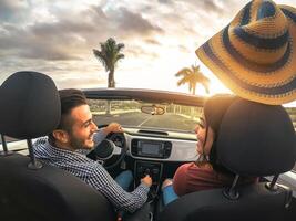 na moda rico casal tendo Diversão dirigindo conversível carro às pôr do sol - feliz romântico amantes desfrutando seus estrada viagem dentro cabriolet auto - amor, relação e juventude romance feriados estilo de vida foto