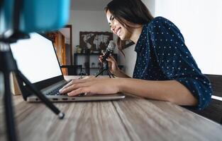 feliz mulher filmando vídeo podcast com inteligente telefone Câmera enquanto usando computador - jovem menina tendo Diversão dentro viver transmissão em social redes - juventude pessoas estilo de vida e tecnologia conceito foto