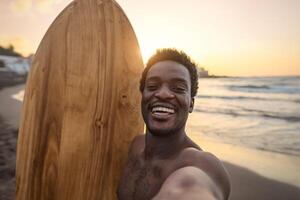 feliz afro surfista tendo Diversão levando selfie durante pôr do sol Tempo - africano homem desfrutando surfar dia - extremo esporte estilo de vida pessoas conceito foto