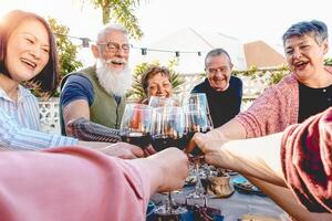 feliz Senior amigos brindar com vermelho vinho óculos às jantar em pátio - maduro pessoas tendo Diversão jantar juntos lado de fora - idosos estilo de vida, Comida e bebida, aposentado e aposentados conceito foto