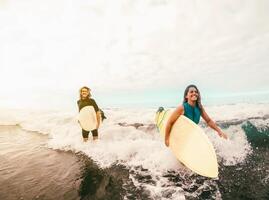 surfistas casal corrida juntos com pranchas de surf em oceano às pôr do sol Tempo - desportivo em forma amigos tendo Diversão surfar em Alto ondas - viagem e extremo esporte cultura estilo de vida conceito foto