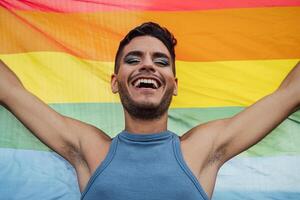 feliz homossexual homem a comemorar gay orgulho segurando arco Iris bandeira símbolo do lgbtq comunidade foto