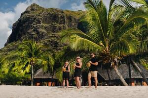 uma à moda família dentro Preto roupas com cocos dentro seus mãos em a de praia do a ilha do maurício.linda família em a ilha do Maurícia dentro a indiano oceano foto