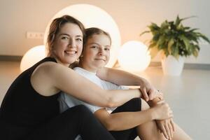 retrato do uma mãe e filha do uma adolescente dentro Esportes roupas abraçando, quem estão juntos dentro uma ginástica sala. a conceito do família Esportes foto