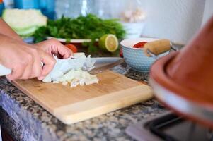 dona de casa mãos fatiamento e cortar cebola em de madeira corte quadro, preparando uma saudável salada para jantar às lar. foto