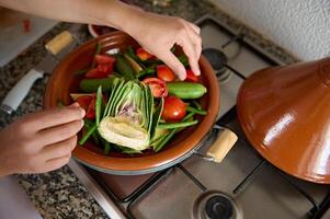 Visão a partir de acima do dona de casa mãos colocando ingredientes enquanto cozinhando tagine com delicioso orgânico legumes foto