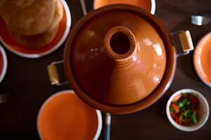 topo Visão argila Panela tagine, recentemente cozido pausa e esvaziar limpar \ limpo laranja pratos em de madeira mesa. marroquino tradicional Comida foto