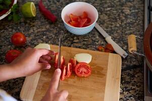 fechar-se Visão a partir de acima do uma dona de casa cortar tomates em uma corte borda foto