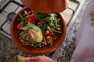 diretamente acima fresco batatas, verde feijões e Alcachofra vapor dentro tradicional argila Panela -tagine, vapor em uma fogão foto