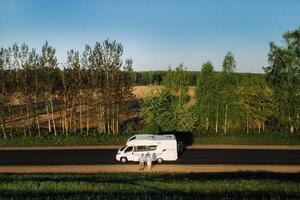 uma casal é em pé em a estrada perto seus motorhome às alvorecer foto