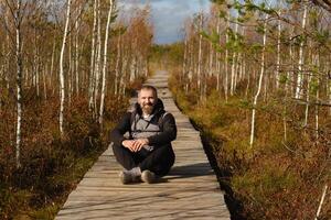 uma homem senta em uma de madeira caminho dentro uma pântano dentro Yelnya, bielorrússia foto