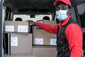 africano Entrega homem Carregando caixas dentro furgão caminhão enquanto vestindo face mascarar para evitar corona vírus espalhar - pessoas trabalhando com velozes entregar durante corona vírus surto foto