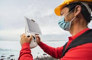 masculino engenheiro monitoramento a zangão inspeção enquanto vestindo face mascarar para evitar corona vírus espalhando - tecnologia e industrial conceito foto