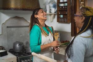 feliz multirracial mulheres tendo Diversão dentro a cozinha preparando uma caseiro receita dentro vintage casa foto