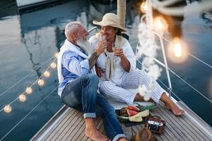 Senior casal brindar champanhe e comendo frutas em barco a vela período de férias - feliz idosos pessoas tendo Diversão a comemorar Casamento aniversário em barco viagem - amor relação e viagem estilo de vida conceito foto