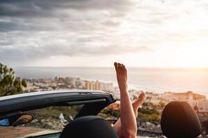 Visão do mulher pernas dentro conversível carro durante uma estrada viagem - jovem menina tendo Diversão viajando dentro cabriolet carro dentro verão período de férias - pessoas, viagem e juventude estilo de vida conceito foto