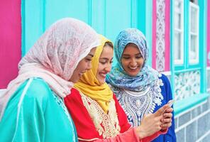 feliz muçulmano mulheres assistindo em Móvel inteligente telefone dentro a Faculdade - árabe jovem meninas tendo Diversão com Novo tecnologias tendências - geração do milênio, geração z e tecnologia conceito foto