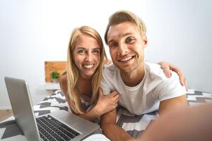 jovem casal levando selfie dentro cama - feliz amantes tendo Diversão levando auto fotos deitado em cama enquanto usando computador portátil dentro quarto - amor relação e juventude cultura estilo de vida conceito