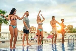 grupo do feliz amigos fazer uma piscina festa às pôr do sol - jovem pessoas tendo Diversão dançando Próximo para a piscina dentro uma tropical luxo recorrer - férias, verão feriados conceito foto