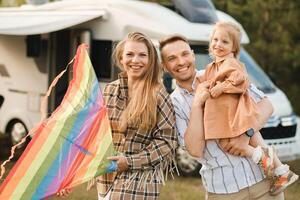 feliz pais com seus criança jogar com uma pipa perto seus motorhome dentro a floresta foto