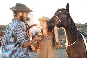 feliz casal tendo Diversão com cavalos dentro estábulo - jovem agricultores partilha Tempo com animais dentro curral rancho - humano e animais relação estilo de vida conceito foto