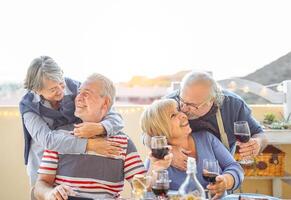 feliz Senior amigos tendo Diversão bebendo vermelho vinho dentro terraço ao ar livre - Mais velho pessoas desfrutando jantar e rindo juntos - amizade e idosos estilo de vida conceito foto