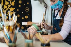 mulher oleiro pintura argila Panela dentro oficina durante corona vírus surto - artesão trabalhos e criativo construir conceito foto