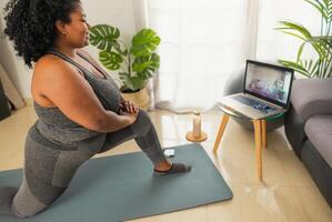 jovem africano mulher fazendo pilates virtual ginástica classe com computador portátil às casa - esporte bem estar pessoas estilo de vida conceito foto