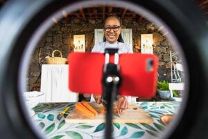feliz afro Senior mulher preparando Comida receita enquanto transmissão conectados com Móvel Smartphone cam para rede cozinha classe mestre canal foto