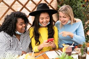 jovem multirracial mulheres assistindo em Móvel Smartphone enquanto tendo saudável almoço dentro café Escovar Barra durante corona vírus surto - Comida e tecnologia conceito foto