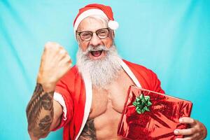 feliz em forma santa claus segurando Natal presente - hipster Senior tendo Diversão a comemorar x-mas feriados - idosos pessoas e tradicional estilo de vida cultura foto