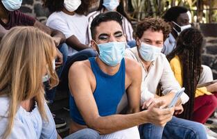 jovem multirracial grupo do amigos sentado em urbano escadas vestindo cirúrgico mascarar - juventude milenar estilo de vida conceito foto