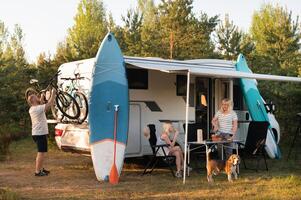 uma feliz família é em repouso perto perto seus motorhome dentro a floresta foto