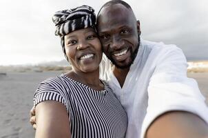 feliz africano casal levando selfie em a de praia com Móvel Smartphone Câmera durante verão período de férias - amor relação conceito foto