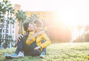 feliz gay casal abraçando e rindo juntos sentado em Relva dentro uma parque - jovem mulheres lésbicas tendo uma concurso momento ao ar livre - lgbt, bissexualidade, relacionamento estilo de vida conceito foto