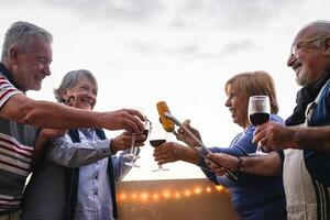 feliz Senior amigos jantar e bebendo vermelho vinho em casa terraço - maduro pessoas tendo Diversão rindo juntos às jantar festa - Comida e idosos amizade estilo de vida conceito foto