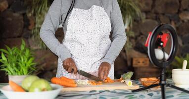 africano mulher preparando Comida receita enquanto transmissão conectados com Móvel Smartphone cam para rede cozinha classe mestre canal foto