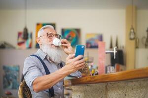 Senior homem usando Móvel Smartphone enquanto bebendo café dentro Barra restaurante - tecnologia e idosos pessoas estilo de vida conceito foto