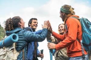 grupo do amigos empilhamento mãos em pico do montanha - jovem turistas caminhada e explorando a selvagem natureza - caminhante, equipe, caminhar e viagem pessoas conceito foto