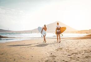 feliz surfistas corrida com pranchas de surf em a de praia - desportivo casal tendo Diversão surfar juntos às pôr do sol - extremo esporte, relação, pessoas e juventude estilo de vida conceito foto