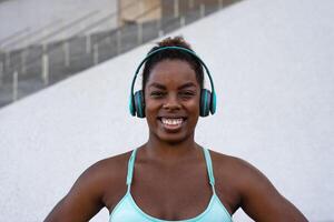 jovem africano em forma mulher ouvindo música com fones de ouvido durante exercite-se sessão ao ar livre - esporte pessoas estilo de vida conceito foto