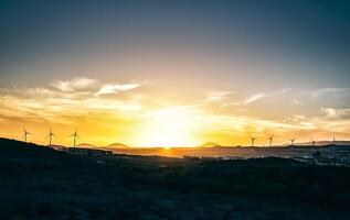 panorâmico Visão do uma pôr do sol sobre colinas com montanhas e vento turbinas dentro a fundo - vinheta editar dentro a céu - cênico panorama verde energia em rural configuração foto